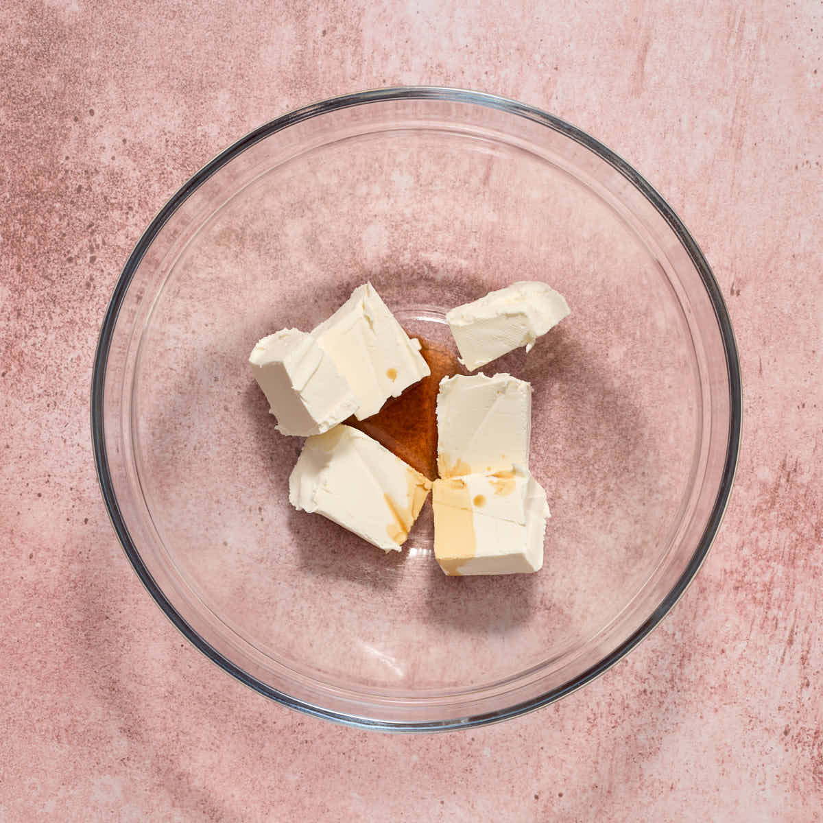 Cubed up cream cheese in a glass bowl with vanilla.