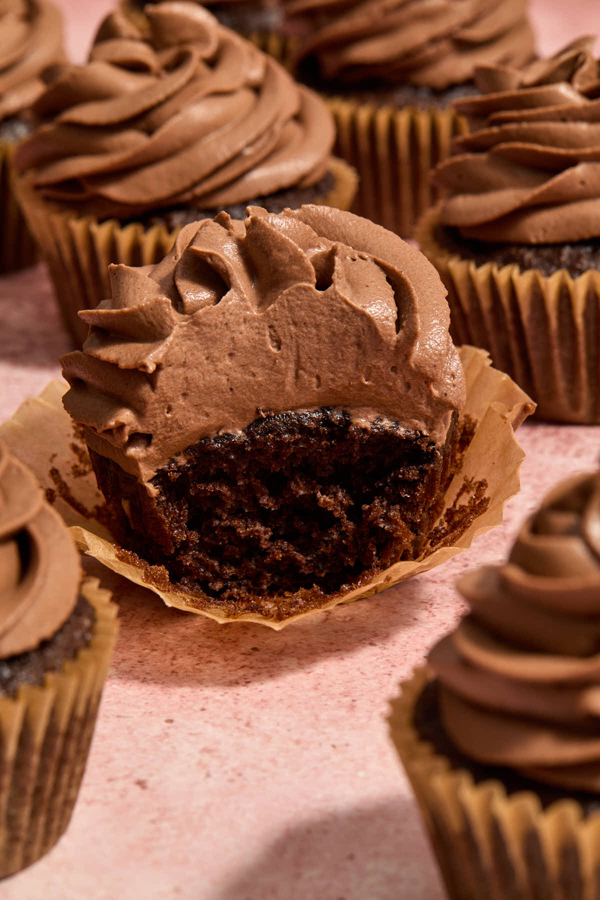 A chocolate cupcake topped with chocolate whipped cream frosting on a parchment wrapper with a bite removed.