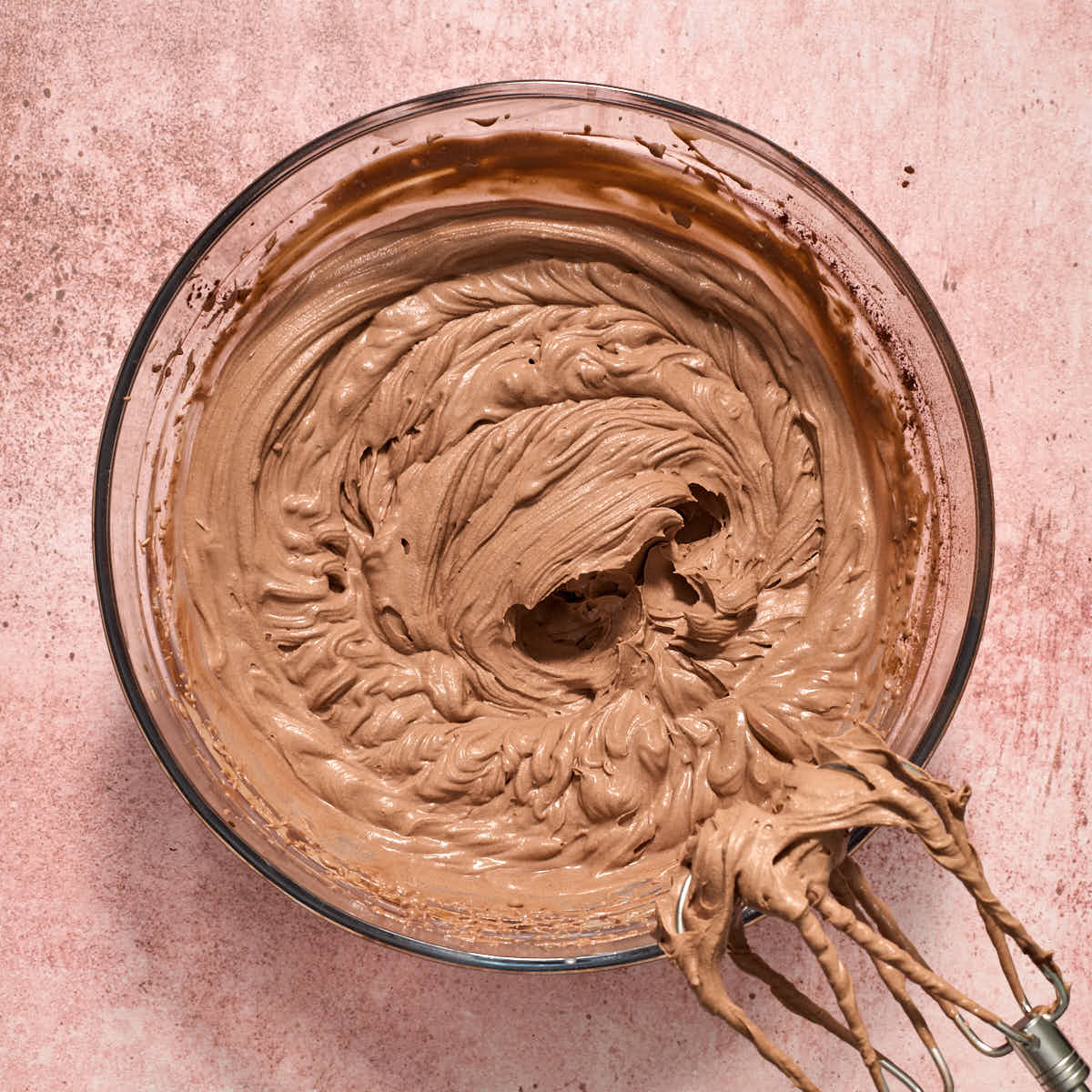 Stiff peaks formed in the chocolate whipped cream cheese frosting in a glass bowl.
