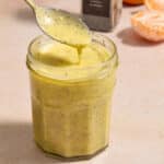 Orange poppy seed dressing in a jar with a spoon lifting some out.