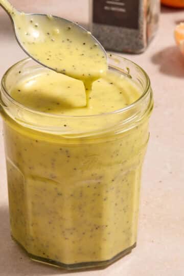 Orange poppy seed dressing in a jar with a spoon lifting some out.