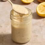 Tahini caesar dressing in a glass jar with a spoonful being lifted out.