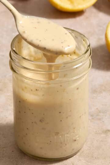 Tahini caesar dressing in a glass jar with a spoonful being lifted out.