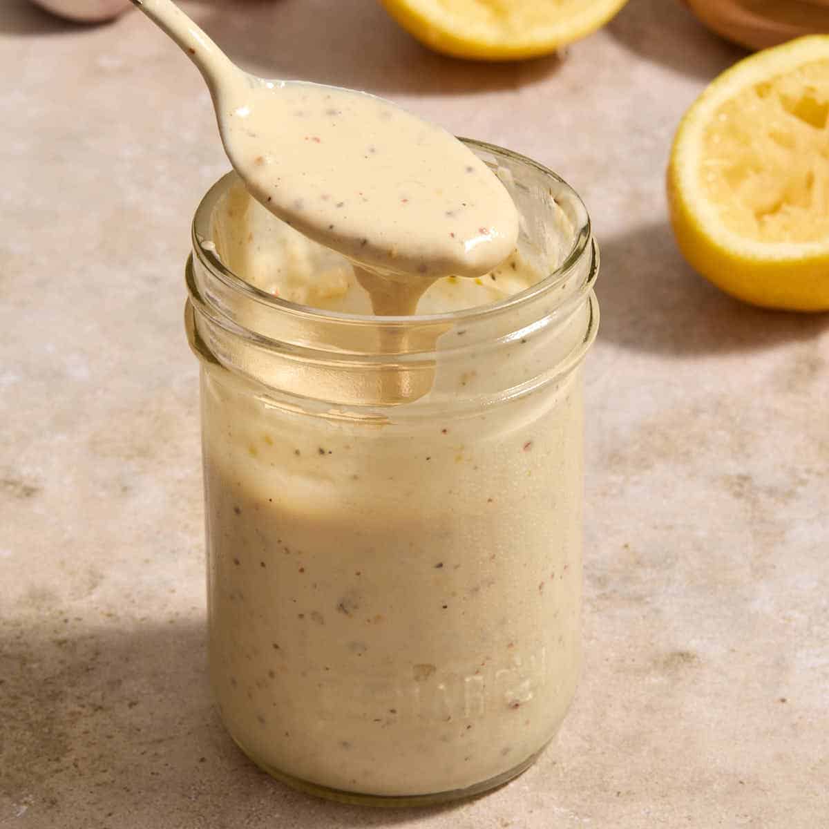 Tahini caesar dressing in a glass jar with a spoonful being lifted out.