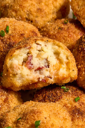 Air fryer mashed potato balls on a plate with a bite removed from one.