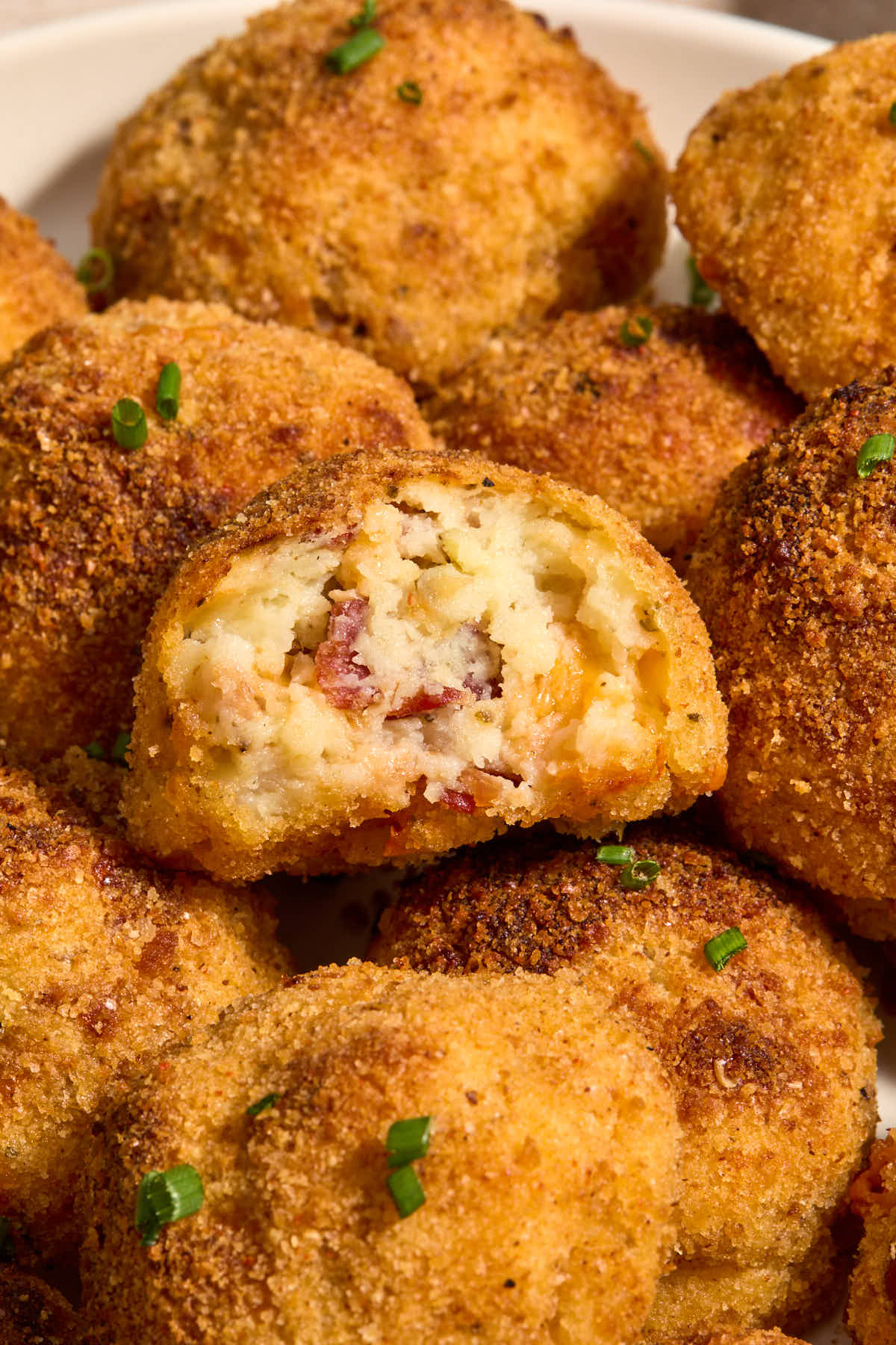 Potato balls piled on a plate with a bite taken out of one.