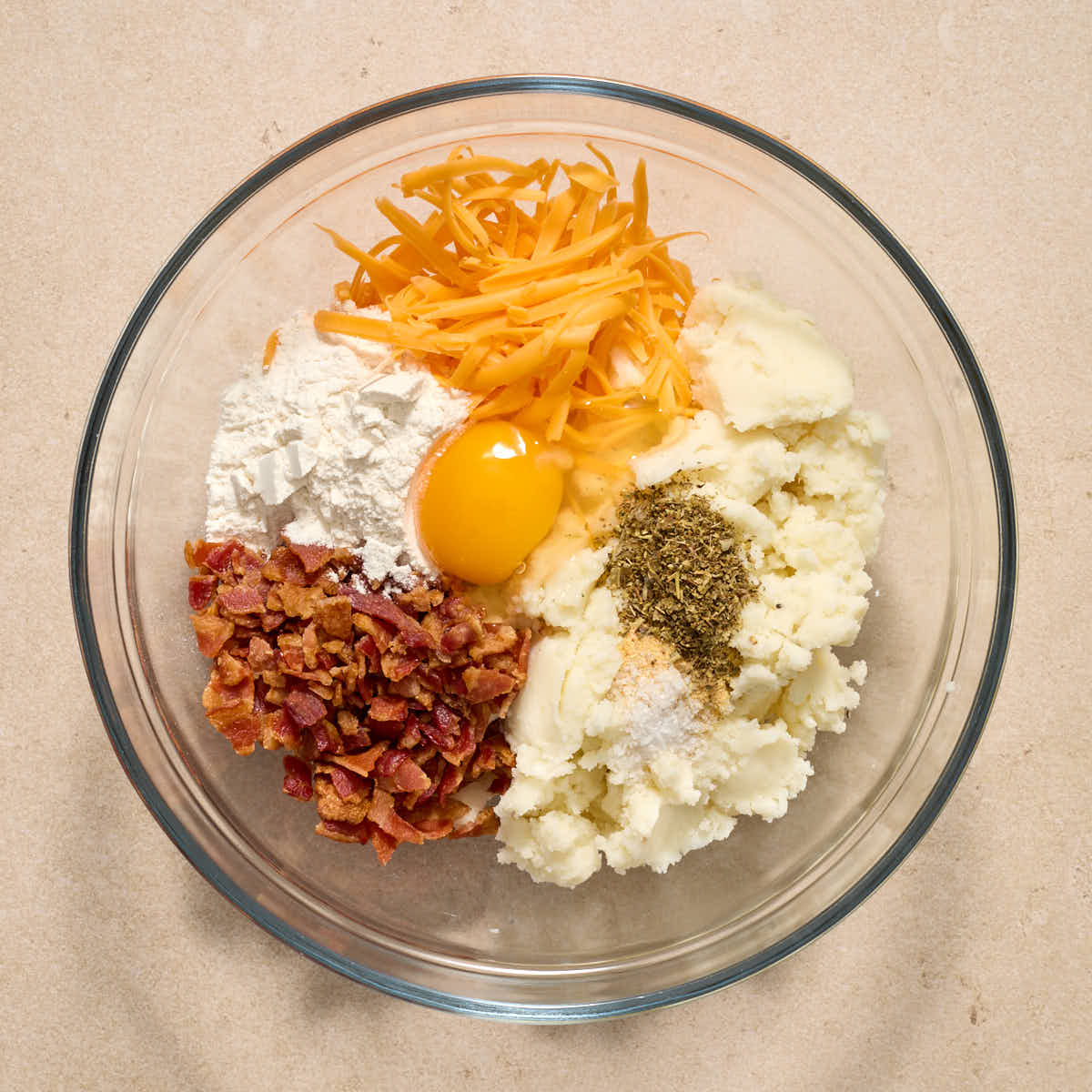 Leftover mashed potatoes, bacon, cheese and other ingredients added to a glass bowl.