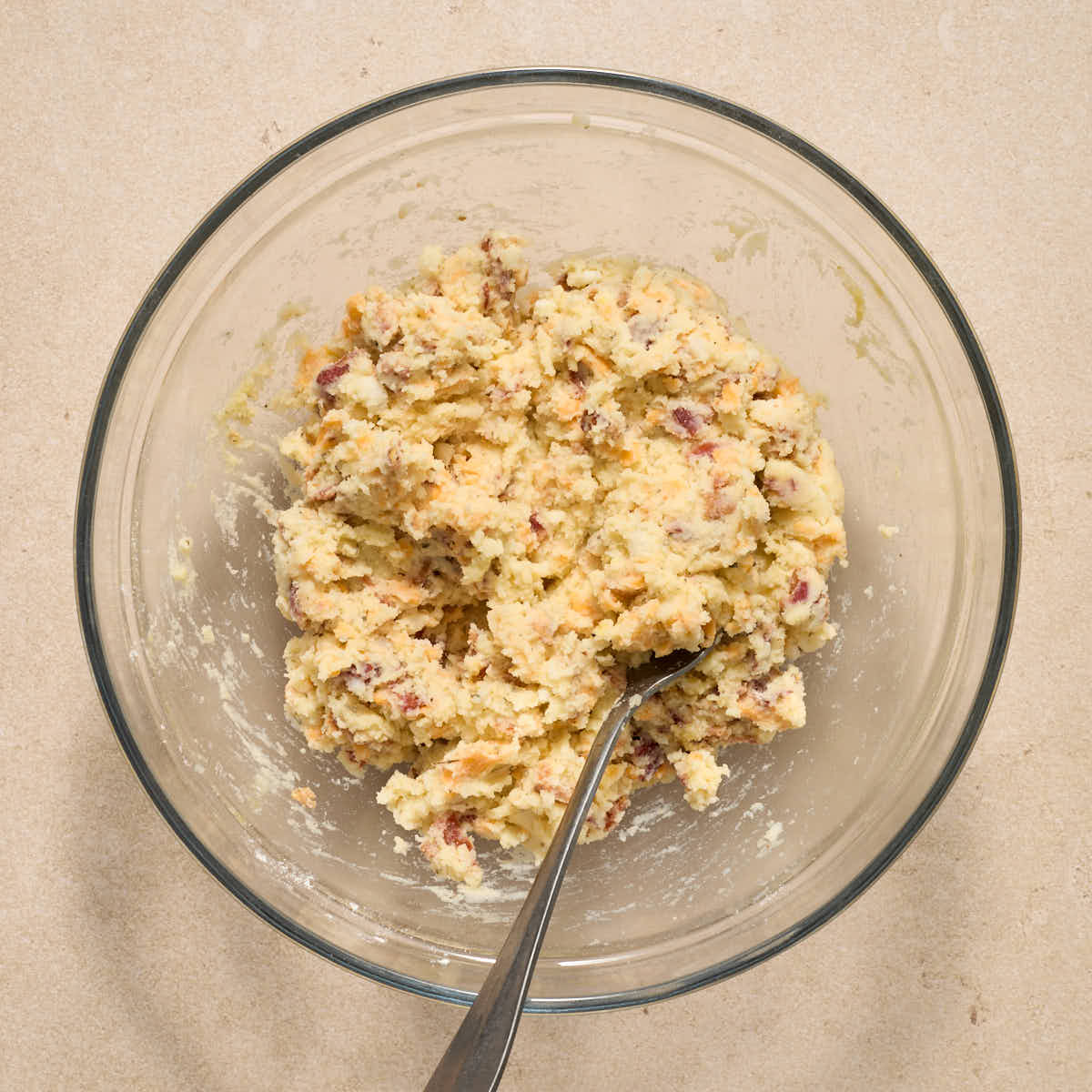 Mashed potato mixture mixed together in a glass bowl with a fork.