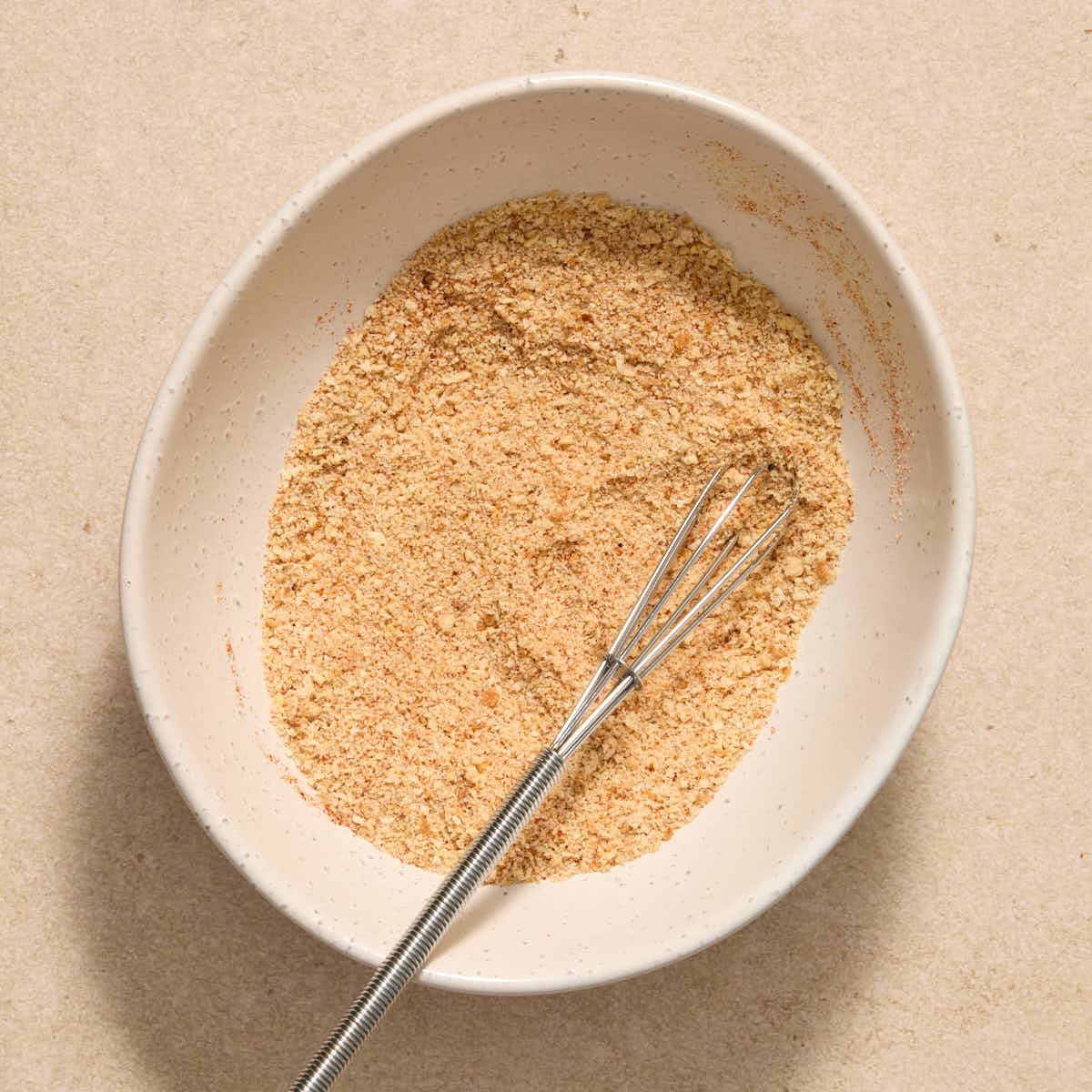 Breadcrumbs and paprika whisked together in a small white bowl.