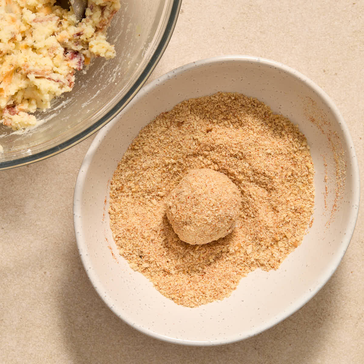 A potato ball rolled in the breadcrumb mixture in a white bowl.