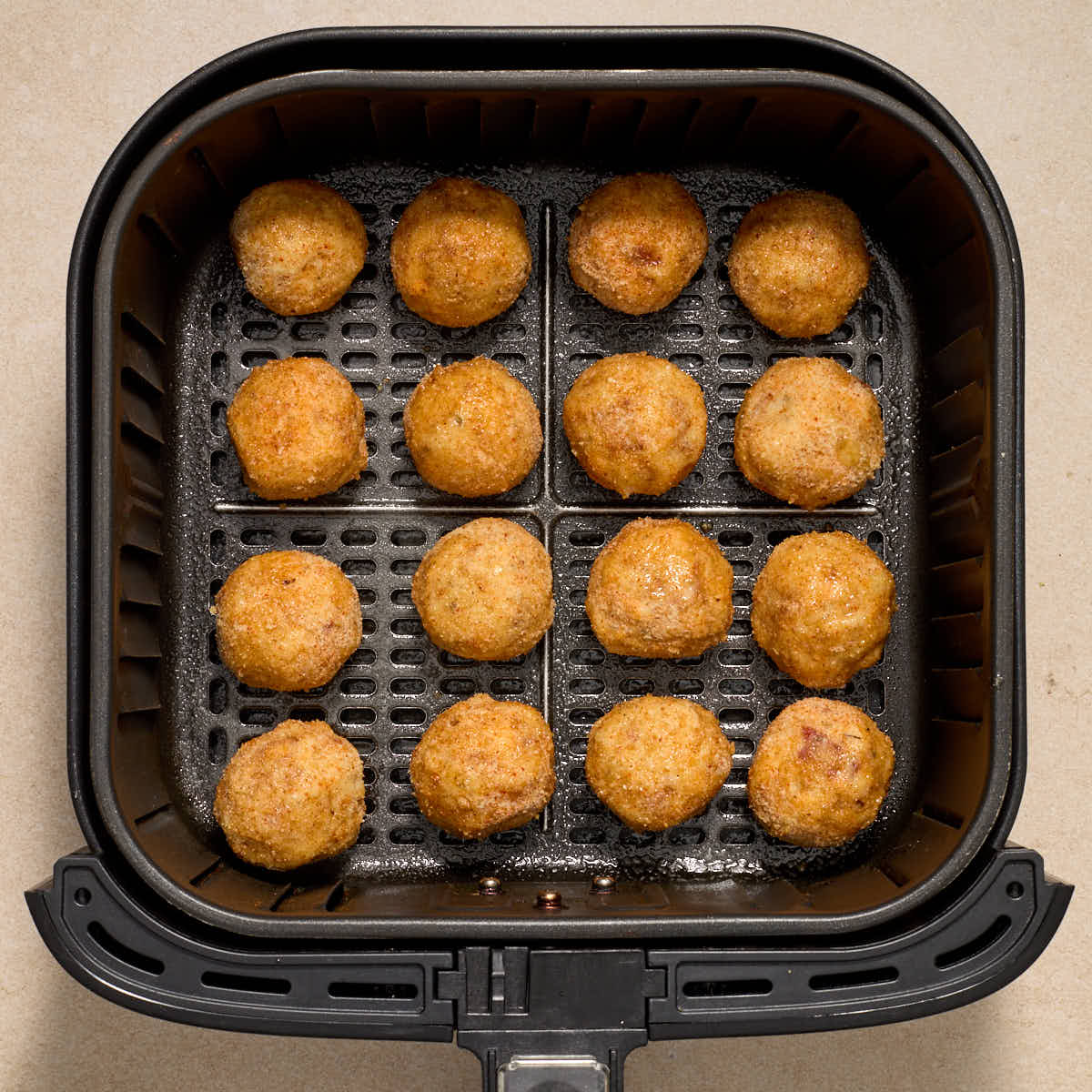 Breaded potato balls arranged in a single layer in an air fryer basket.