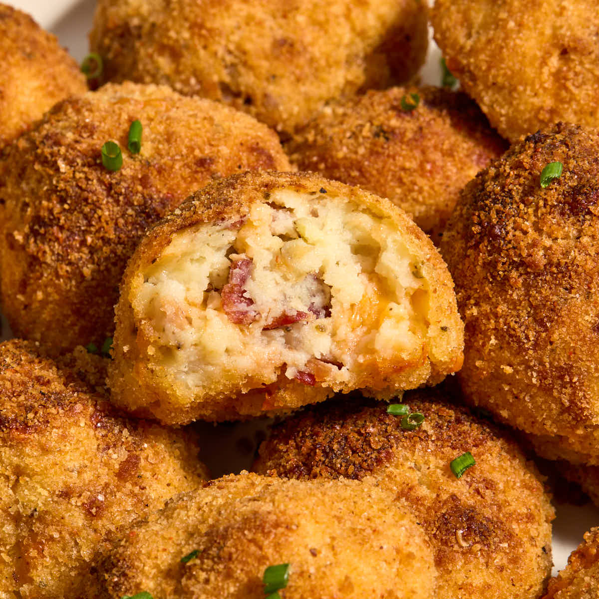 Air fryer mashed potato balls on a plate with a bite removed from one.