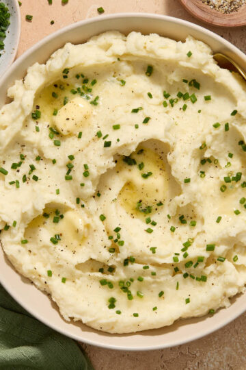 Air fryer mashed potatoes served in a bowl with chopped chives, butter and pepper on top.