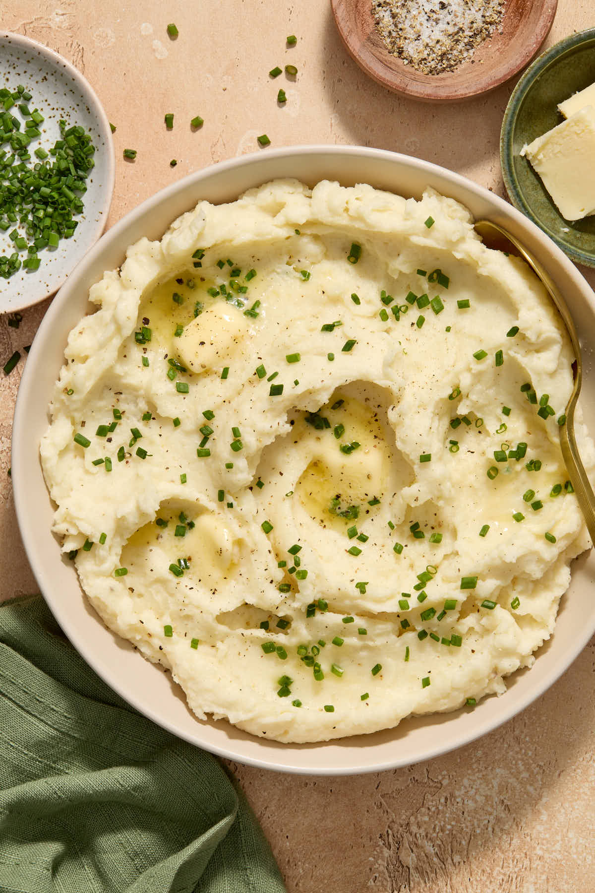 Mashed potatoes served in a bowl with chives, salt and pepper and butter on the side.