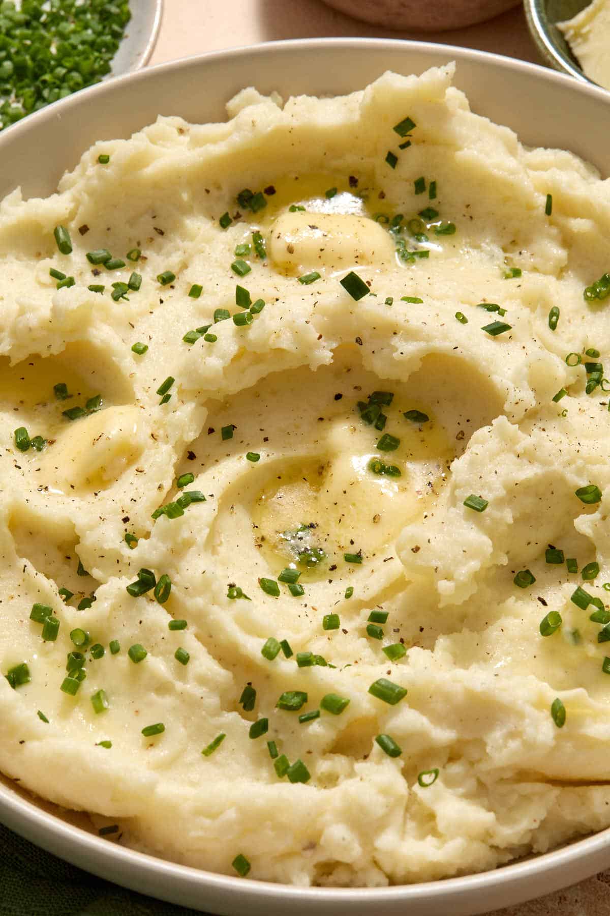 Close up of mashed potatoes in a bowl with melted butter and chives on top.