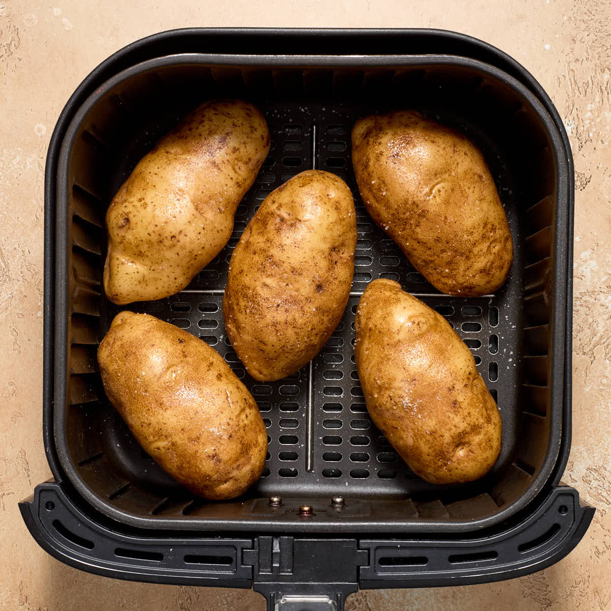 Whole, raw potatoes in an air fryer basket.