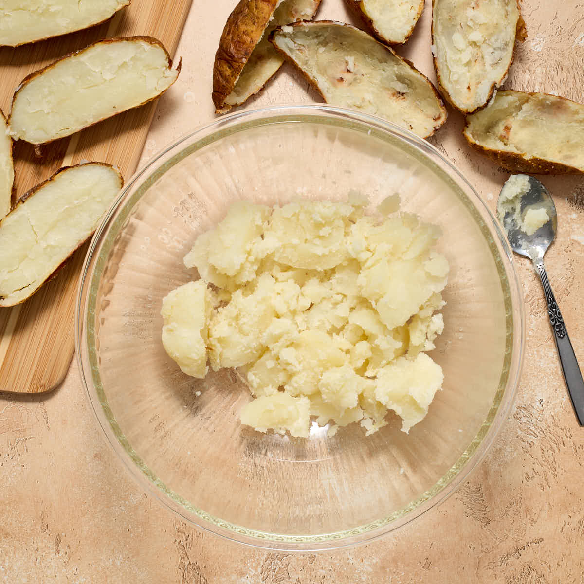 Potato flesh scooped out into a bowl with potato skins on the side.