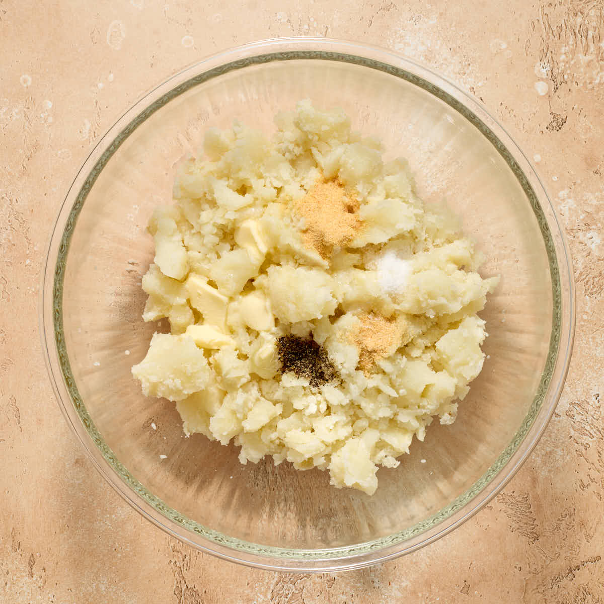 Seasonings and butter added to the bowl of potatoes.