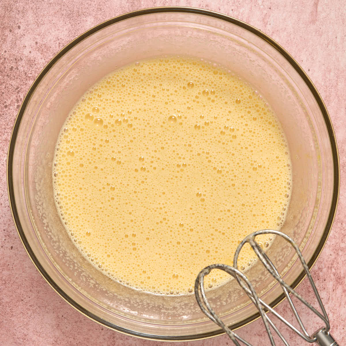 Eggs and sugar beaten together in a glass bowl.