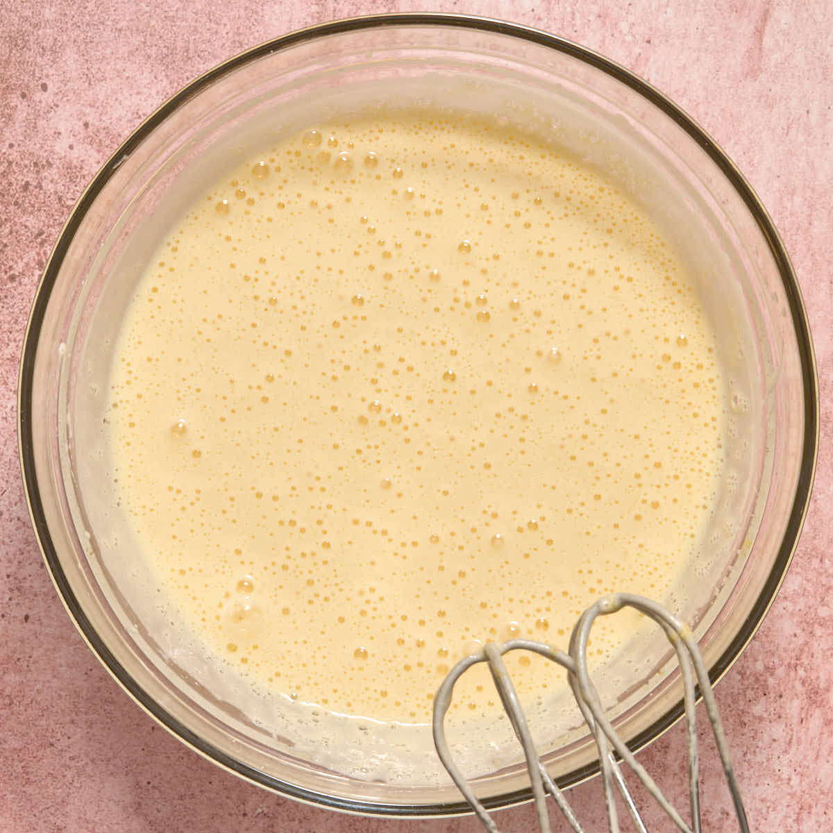 Eggs and sugar beaten together in a glass bowl after 3 minutes, looking pale and thick.