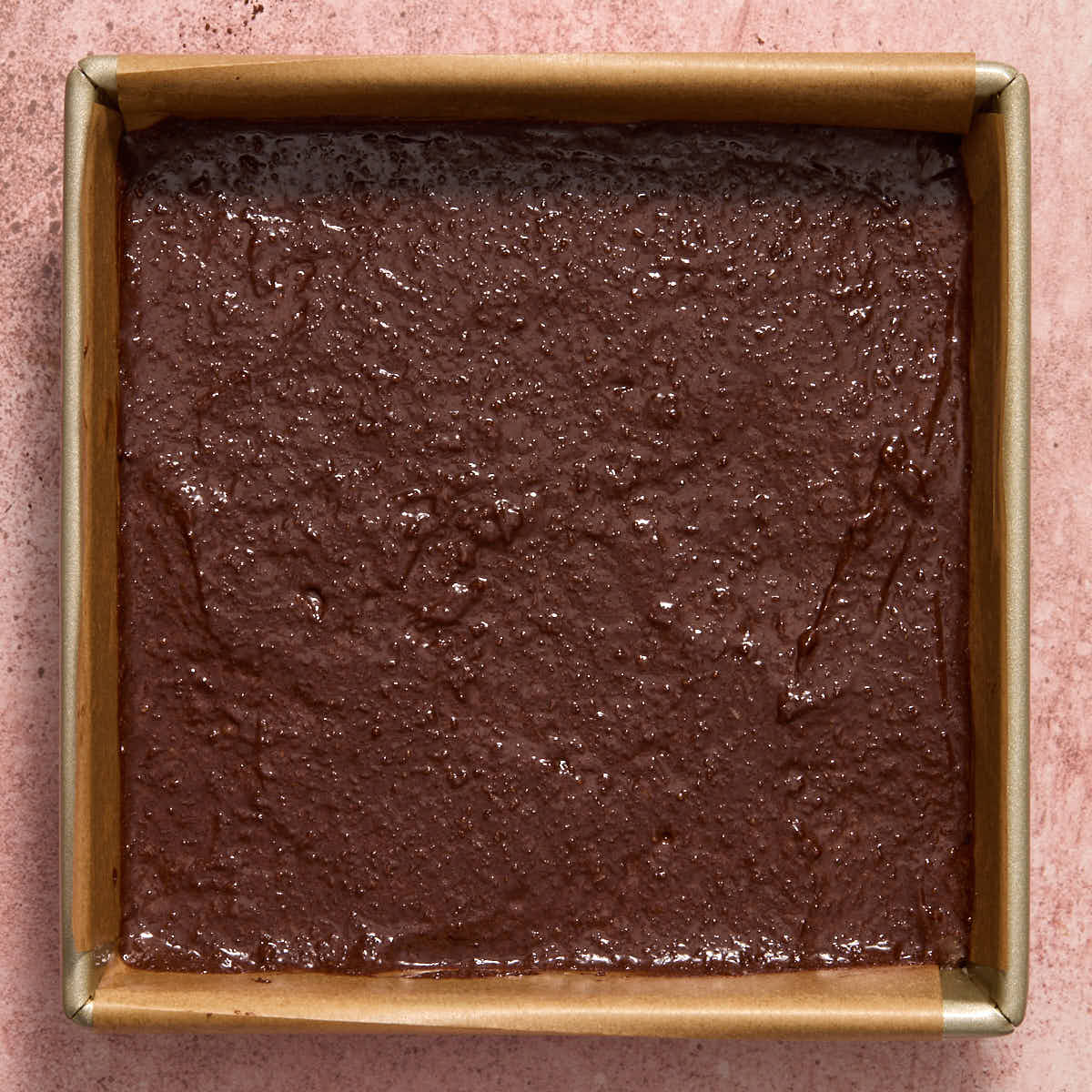 Brownie batter spread out in a square pan lined with parchment paper.