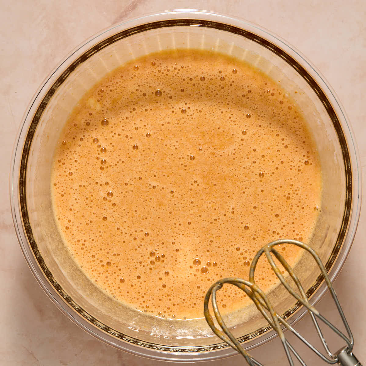 All of the wet ingredients mixed together in a glass bowl with beaters in the frame.