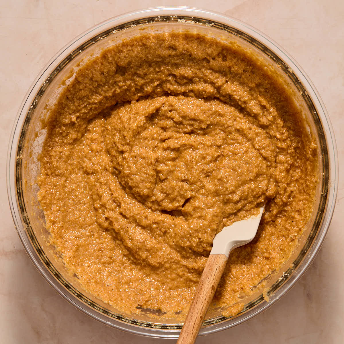 Pumpkin muffin batter mixed together in a large glass bowl with a spatula.