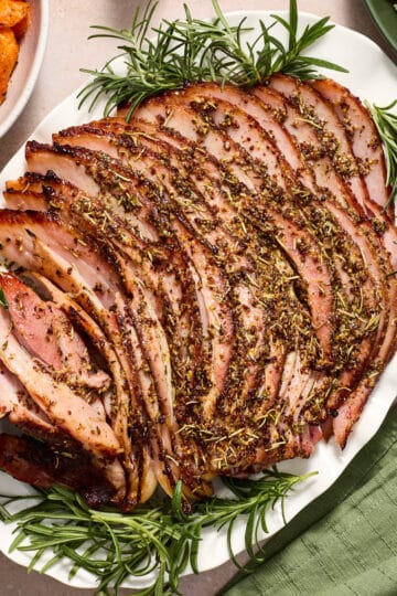 Air fryer ham with savory, sugar-free glaze served on a white platter with fresh herbs.
