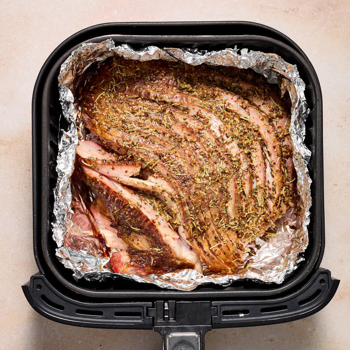 Ham uncovered in air fryer basket with final amount of glaze brushed on.
