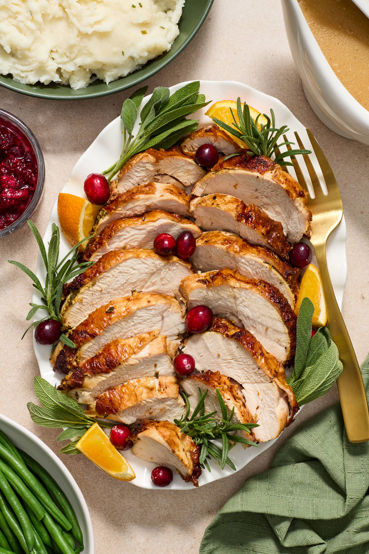Sliced turkey on a white platter with gravy, mashed potatoes and green beans on the side.