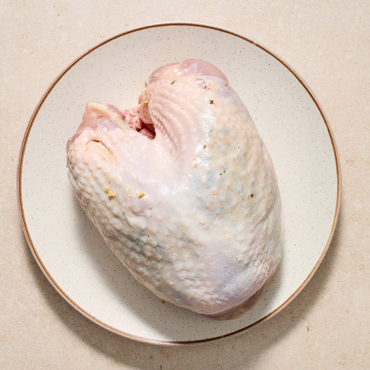 Raw turkey breast on a plate and butter mixture stuffed underneath the skin.