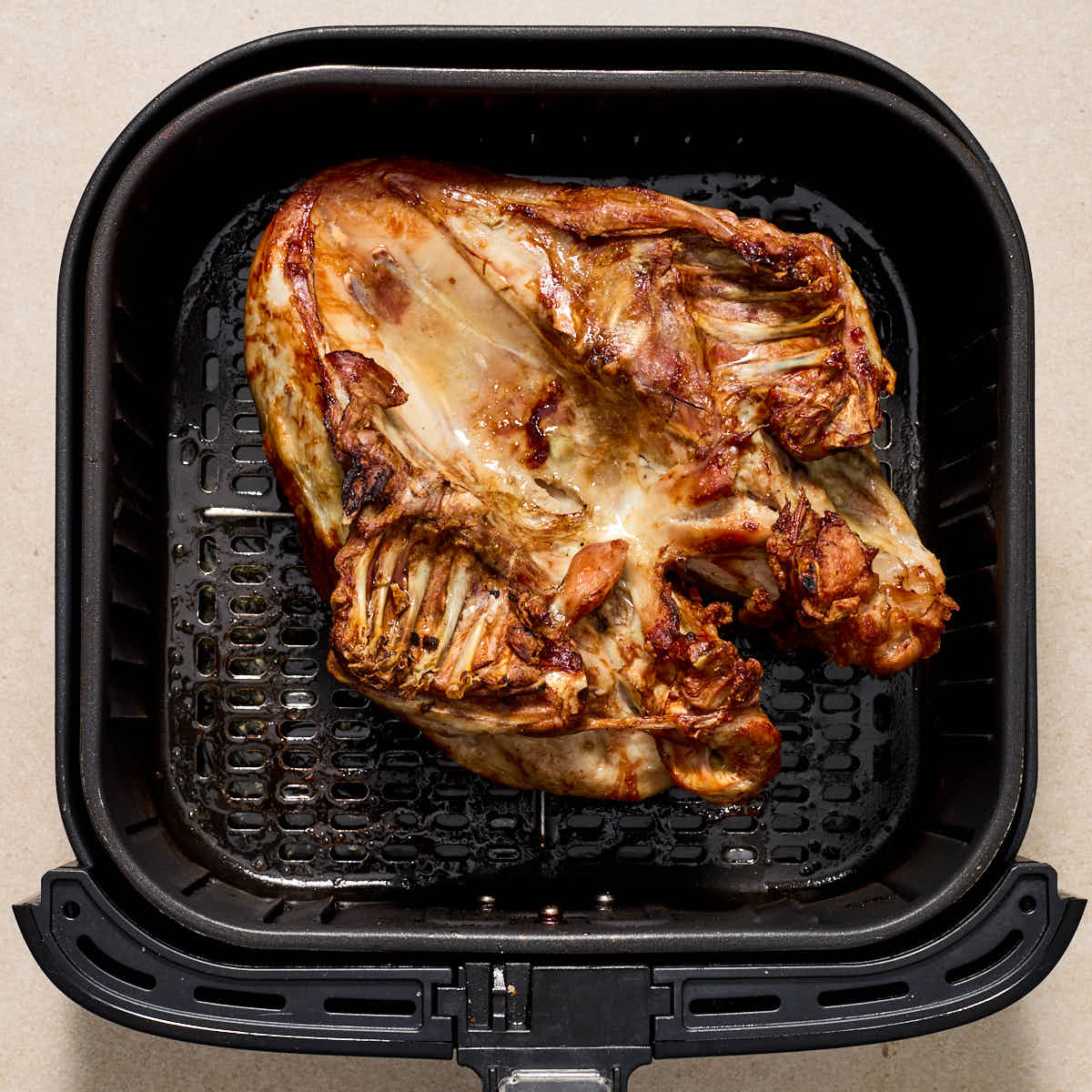 Turkey breast flipped over in the air fryer basket so the breast side is down.