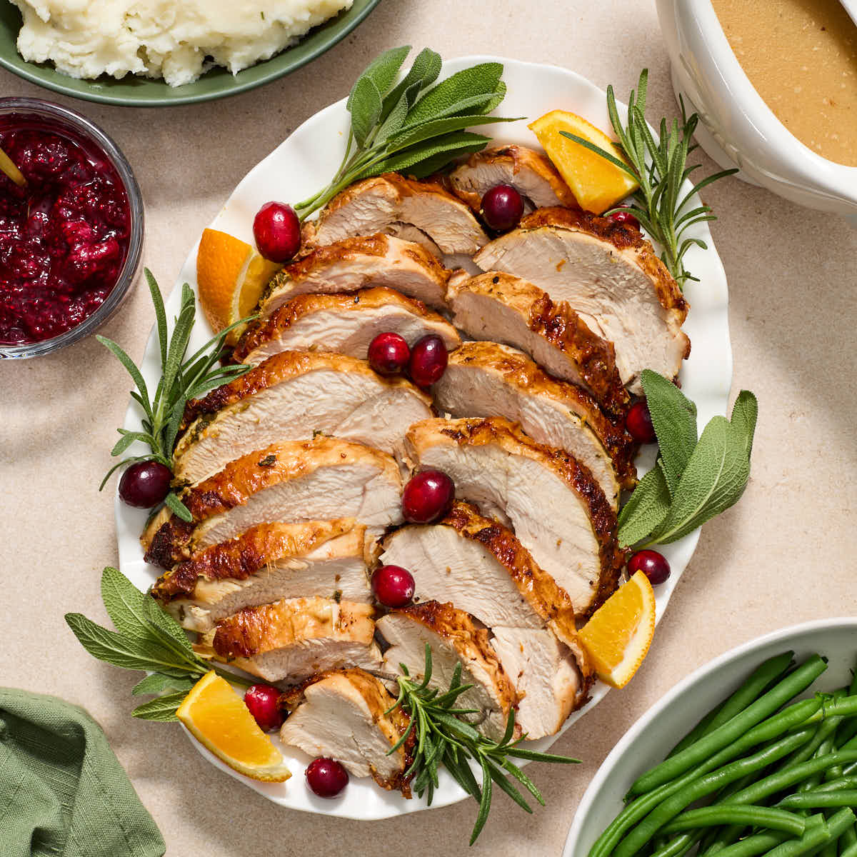 Air fryer turkey breast sliced and served on a platter with fresh herbs, cranberries and orange wedges.